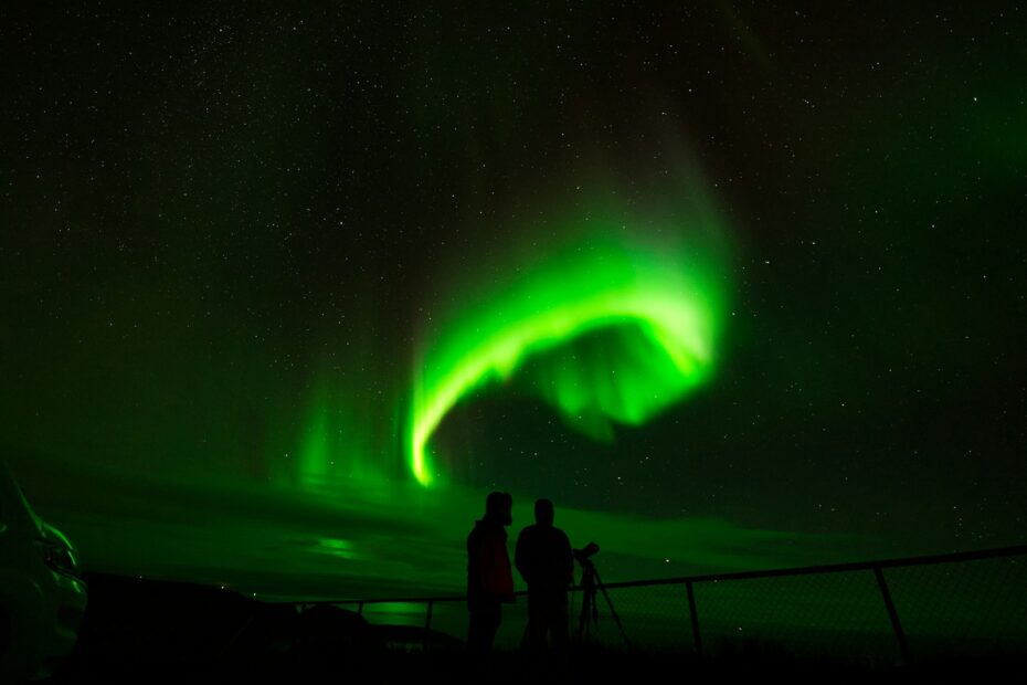 a couple of people standing next to a fence under a green light